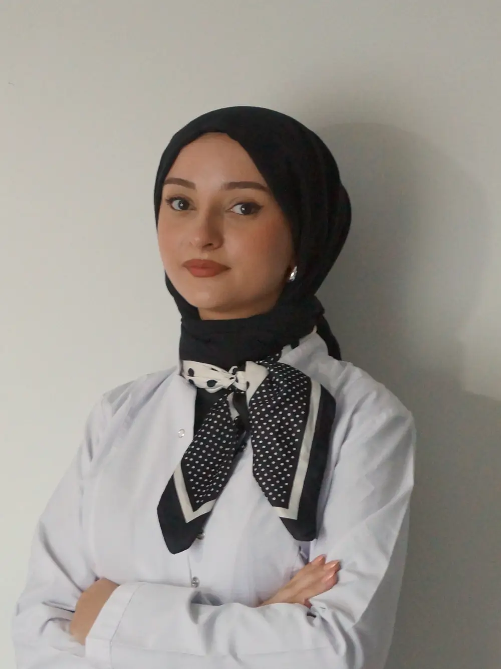 Diyetisyen Yaren Zorlu, beyaz önlüğü ve siyah başörtüsüyle kameraya bakıyor